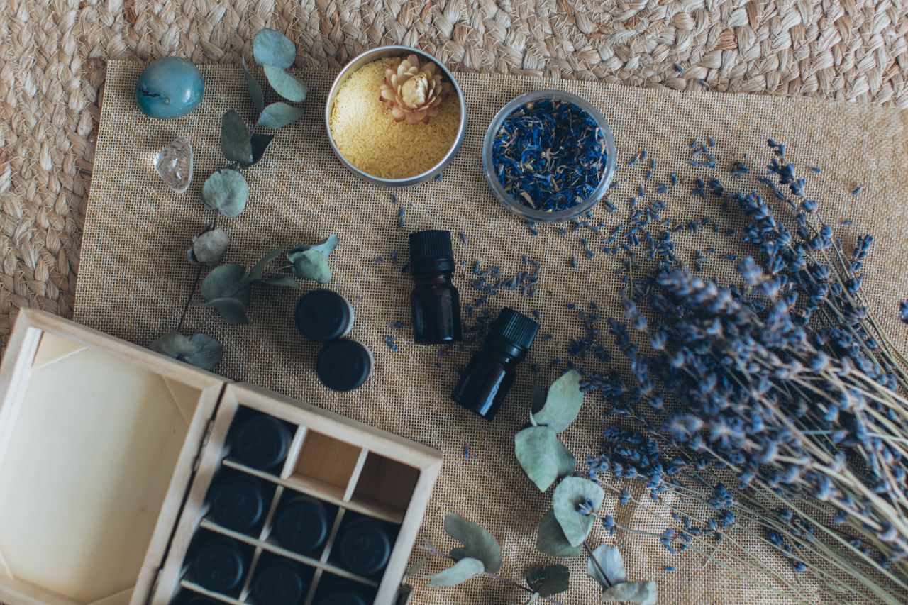 A flat lay displaying essential oils, dried lavender, and other aromatherapy items on a woven mat.