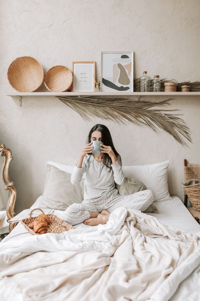 Woman enjoying coffee in a stylish bedroom with cozy decor.